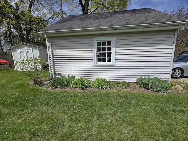 view of side of property with a shingled roof, a yard, an outbuilding, and a storage shed