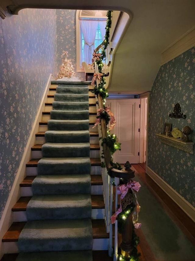 stairway featuring crown molding, vaulted ceiling, wallpapered walls, and wood finished floors