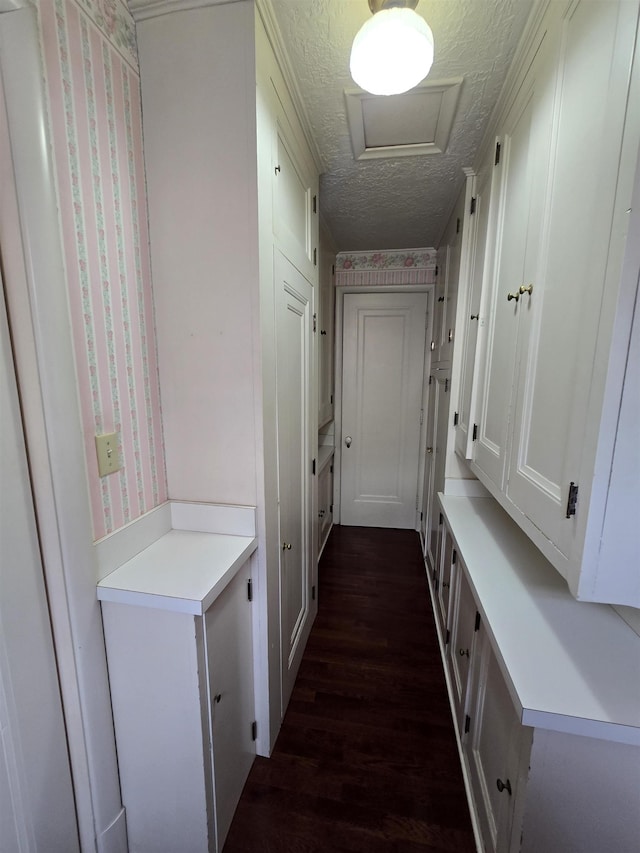 corridor with a textured ceiling, dark wood finished floors, attic access, and wallpapered walls