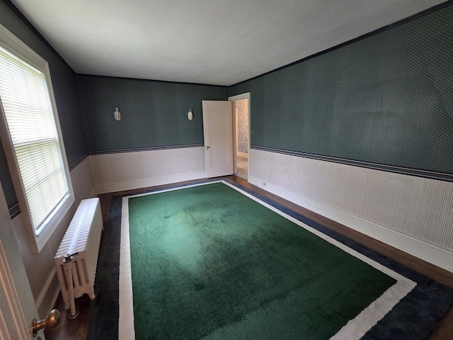 empty room featuring baseboards, radiator, wood finished floors, and a wainscoted wall