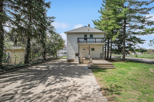 exterior space with driveway, a chimney, fence, a balcony, and a front lawn