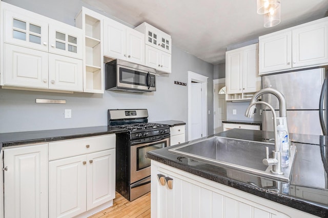 kitchen with stainless steel appliances, open shelves, dark countertops, and a sink