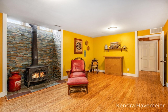 sitting room with baseboards, visible vents, wood finished floors, and a wood stove