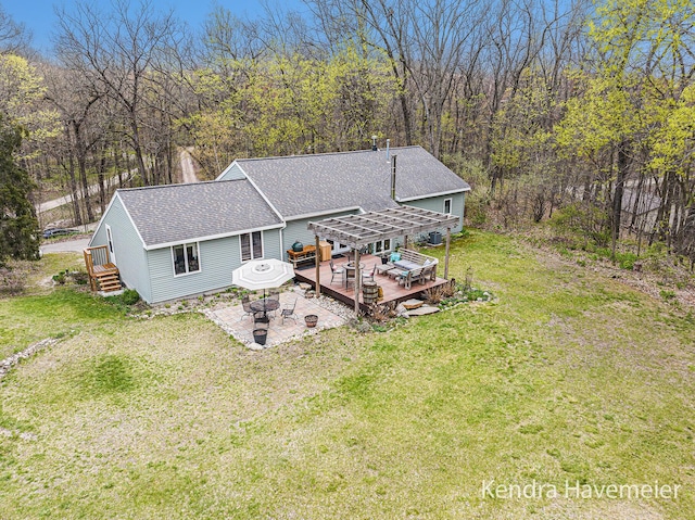 back of property featuring a fire pit, a wooden deck, a pergola, a shingled roof, and a lawn