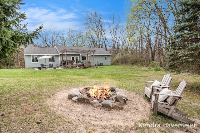 rear view of property with roof with shingles, a wooden deck, a yard, and an outdoor fire pit