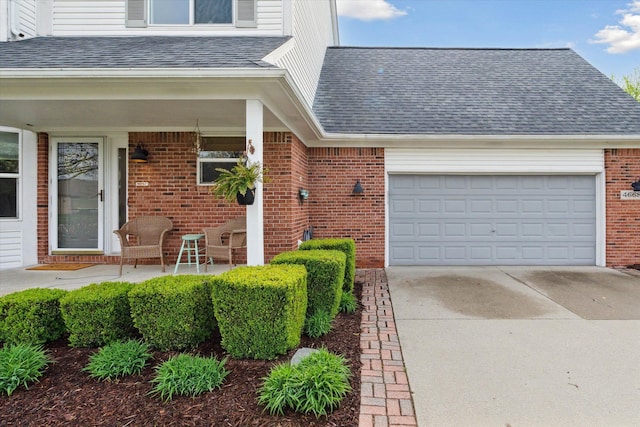 doorway to property featuring brick siding, a shingled roof, an attached garage, and concrete driveway