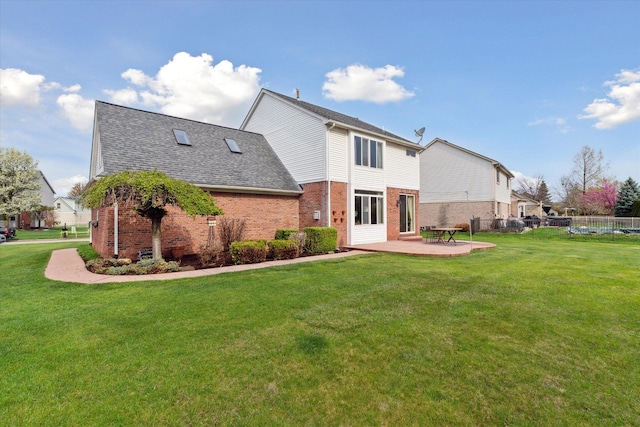 rear view of property with roof with shingles, a lawn, brick siding, fence, and a patio