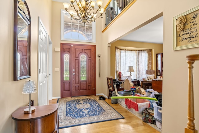 foyer entrance with baseboards, a chandelier, a wealth of natural light, and wood finished floors