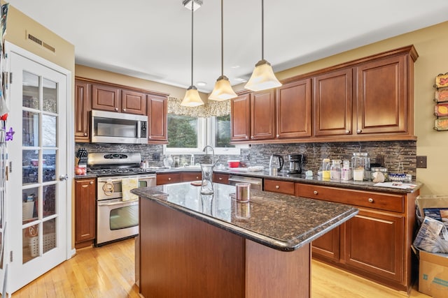 kitchen featuring appliances with stainless steel finishes, light wood finished floors, dark stone countertops, backsplash, and visible vents