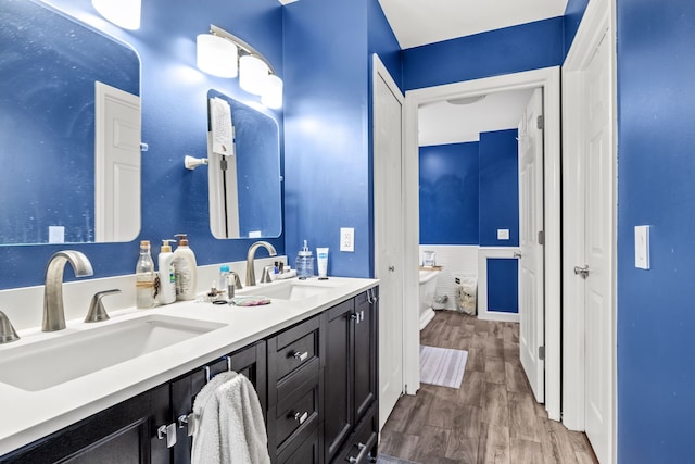 full bathroom with a sink, a freestanding tub, double vanity, and wood finished floors