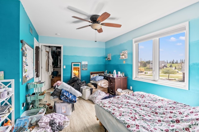 bedroom featuring a walk in closet, a ceiling fan, visible vents, wood finished floors, and a closet