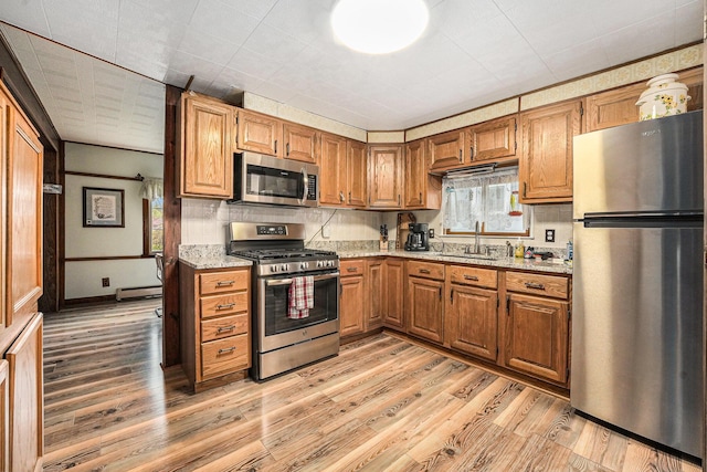kitchen with stainless steel appliances, a baseboard heating unit, a sink, and light wood finished floors