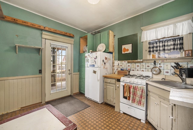 kitchen with a sink, white appliances, light countertops, dark floors, and a wainscoted wall