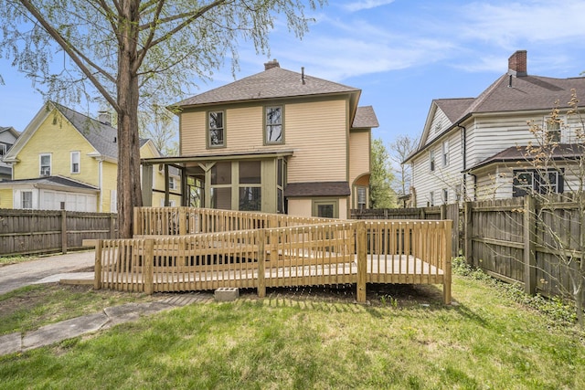 back of property featuring a fenced backyard, a lawn, a wooden deck, and a sunroom