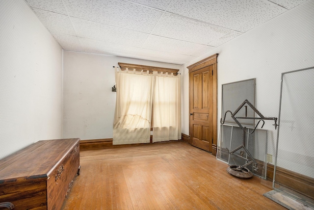 interior space featuring baseboards, a drop ceiling, and hardwood / wood-style flooring