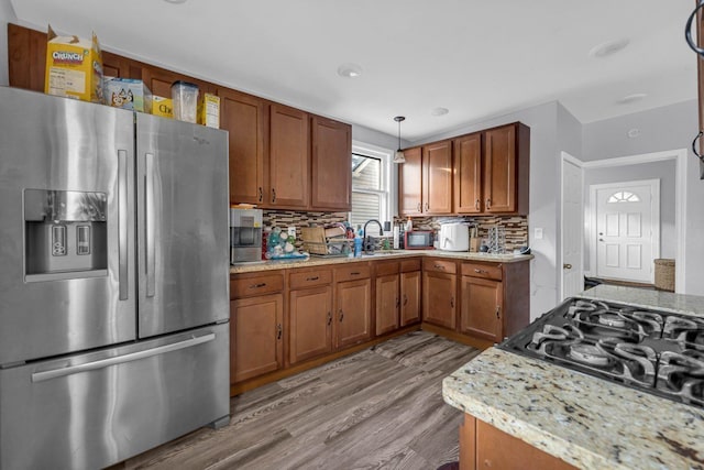 kitchen with decorative backsplash, stainless steel refrigerator with ice dispenser, brown cabinetry, and wood finished floors