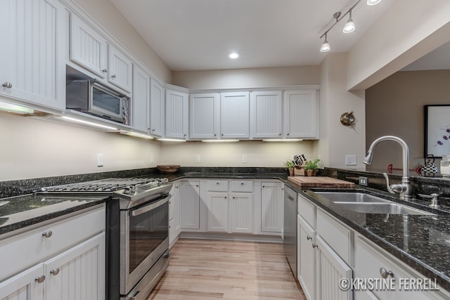kitchen featuring dark stone counters, white cabinets, a sink, light wood finished floors, and appliances with stainless steel finishes
