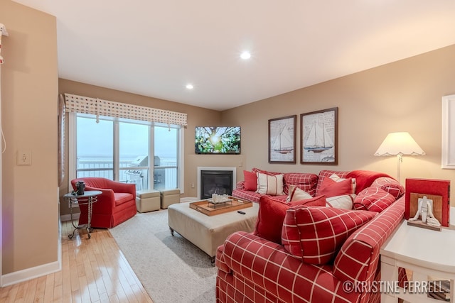living area with light wood-type flooring, recessed lighting, baseboards, and a glass covered fireplace