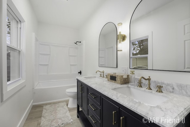 bathroom featuring double vanity, toilet, a sink, and wood finished floors