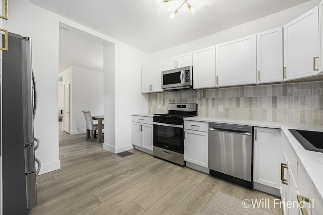 kitchen featuring light wood-style flooring, white cabinets, tasteful backsplash, and stainless steel appliances