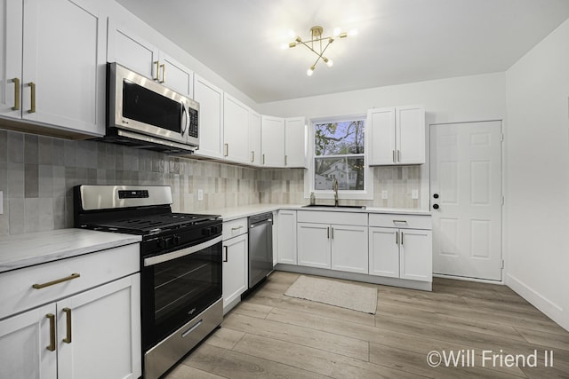 kitchen featuring white cabinets, a sink, light countertops, stainless steel appliances, and backsplash