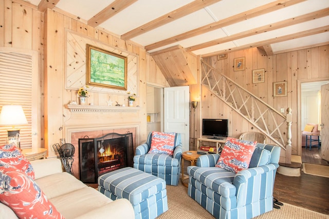 living room featuring wood walls, stairs, wood finished floors, beamed ceiling, and a lit fireplace