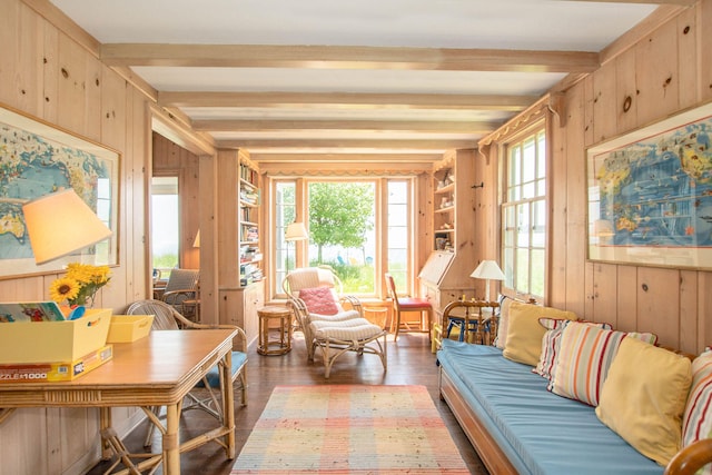 living area featuring beamed ceiling, wood walls, a healthy amount of sunlight, and light wood-style flooring