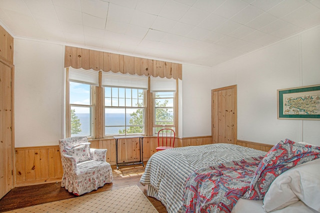 bedroom featuring crown molding, wood walls, wainscoting, and wood finished floors