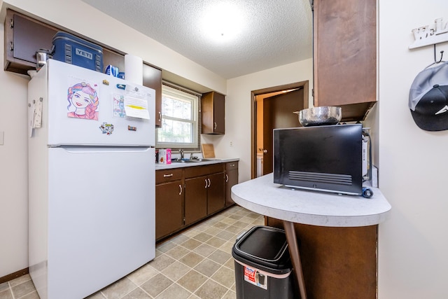 kitchen featuring freestanding refrigerator, a textured ceiling, a sink, and light countertops