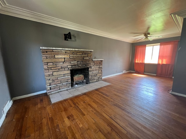 unfurnished living room with crown molding, hardwood / wood-style floors, baseboards, a stone fireplace, and a ceiling fan