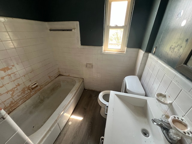 full bathroom featuring tile walls, wood finished floors, a wainscoted wall, toilet, and a tub to relax in