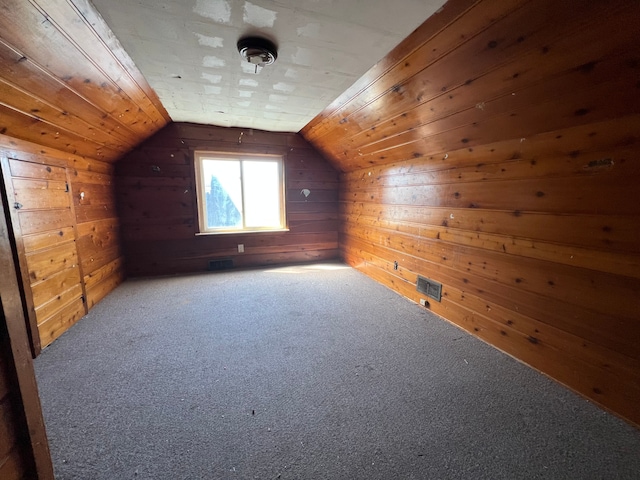additional living space featuring wooden walls, visible vents, carpet flooring, and lofted ceiling