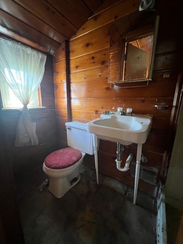 bathroom featuring a sink, wooden walls, vaulted ceiling, and toilet