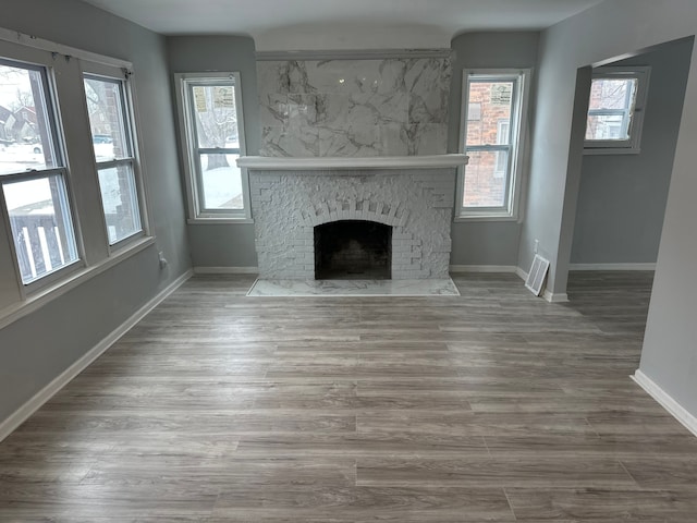 unfurnished living room featuring baseboards, a fireplace, wood finished floors, and visible vents