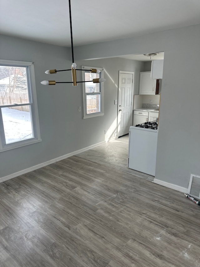 unfurnished dining area featuring an inviting chandelier, baseboards, wood finished floors, and visible vents