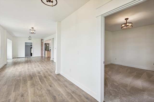 hall featuring baseboards, a chandelier, and light wood-style floors
