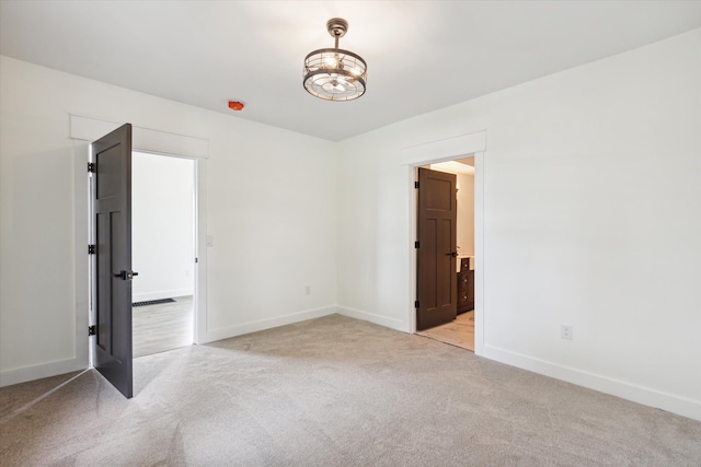 spare room with a chandelier, baseboards, and light colored carpet