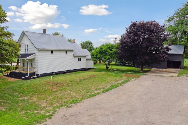 view of home's exterior featuring an outdoor structure, a chimney, dirt driveway, metal roof, and a lawn