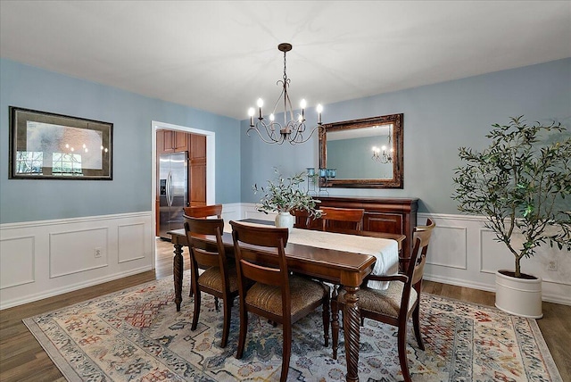 dining area featuring wainscoting, a decorative wall, wood finished floors, and a chandelier