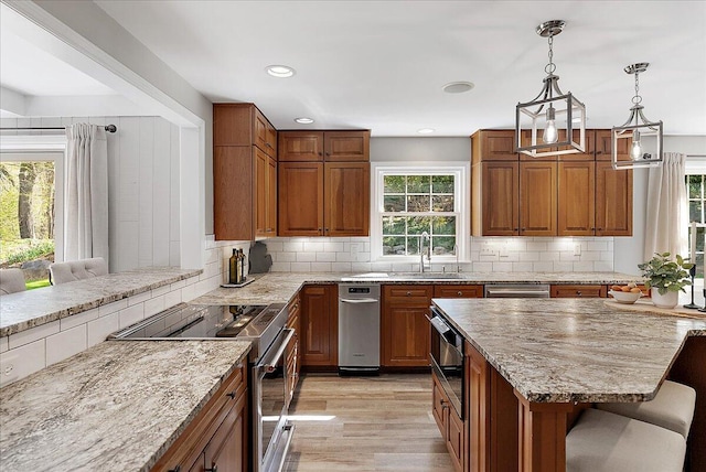 kitchen featuring brown cabinetry, light stone countertops, a sink, stainless steel appliances, and light wood-style flooring