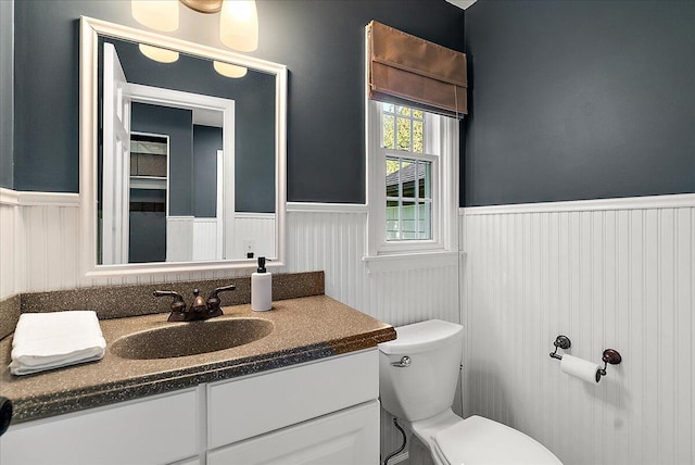 half bath featuring a wainscoted wall, vanity, and toilet