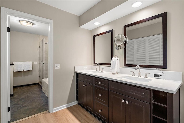 bathroom featuring double vanity, a shower stall, a sink, and wood finished floors