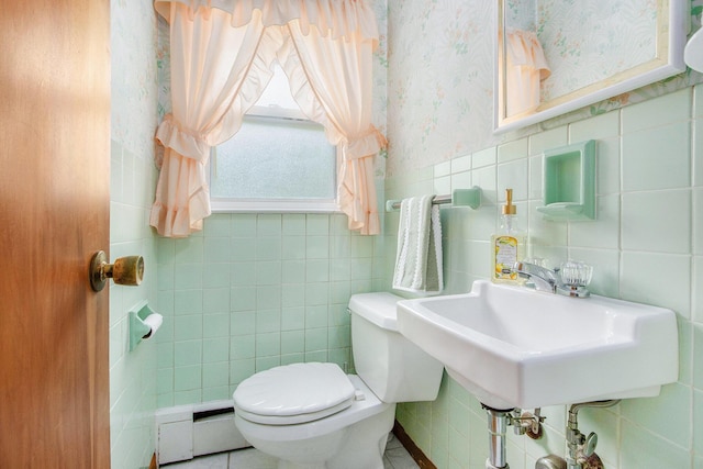 half bath featuring tile walls, a sink, a baseboard radiator, toilet, and wallpapered walls