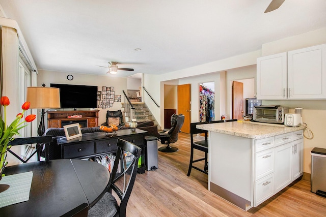 kitchen with a ceiling fan, light wood finished floors, white cabinets, and open floor plan