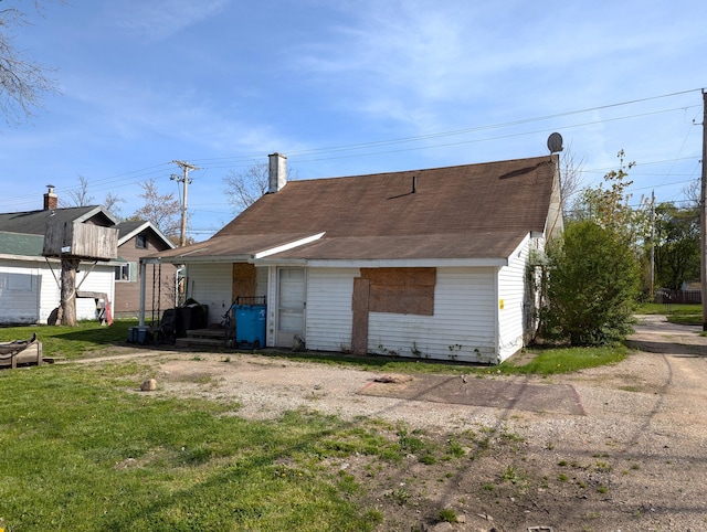 rear view of property with roof with shingles, a chimney, and a yard