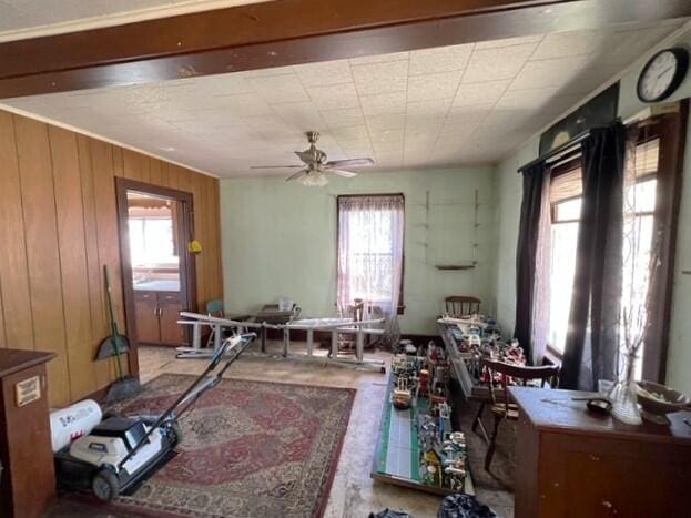 misc room with wooden walls, a ceiling fan, and a wealth of natural light