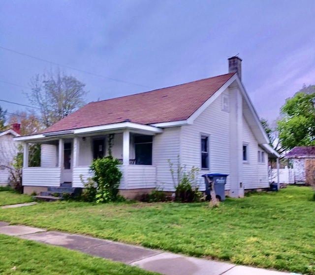 bungalow-style house with a porch, a chimney, roof with shingles, and a front lawn