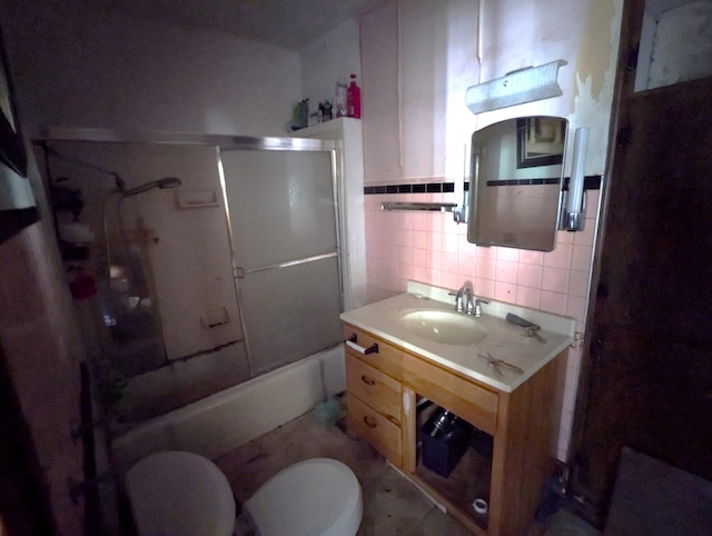 full bathroom with vanity, bath / shower combo with glass door, toilet, and tile walls