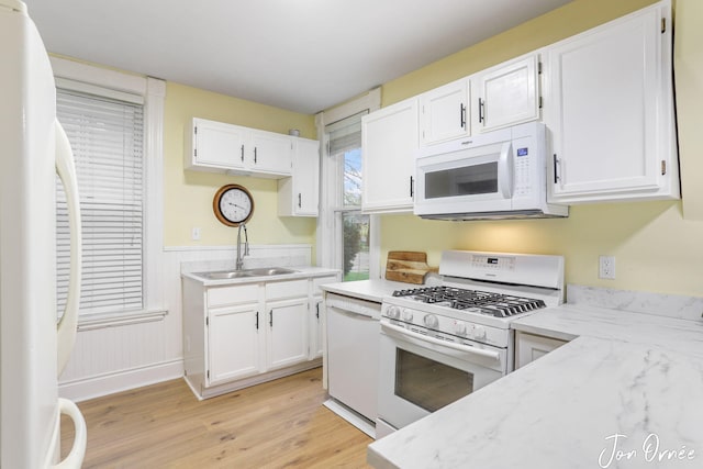 kitchen with white cabinets, wainscoting, a sink, light wood-style floors, and white appliances