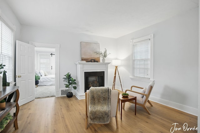 sitting room with visible vents, light wood-style flooring, a glass covered fireplace, and baseboards